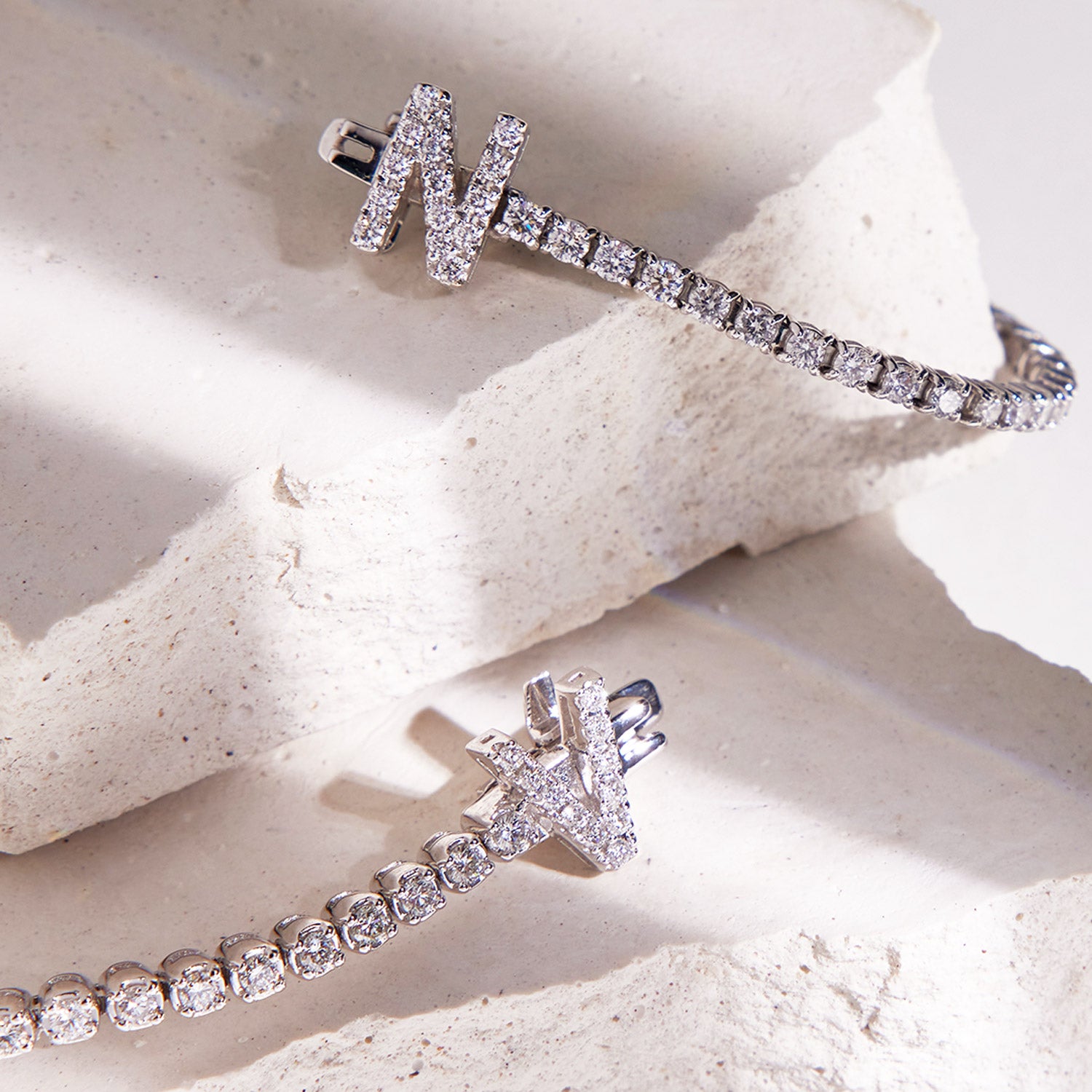 Faith Jewels bespoke initial diamond tennis bracelets in white gold, each featuring a unique clasp shaped as a letter N and V — set with round brilliant-cut diamonds