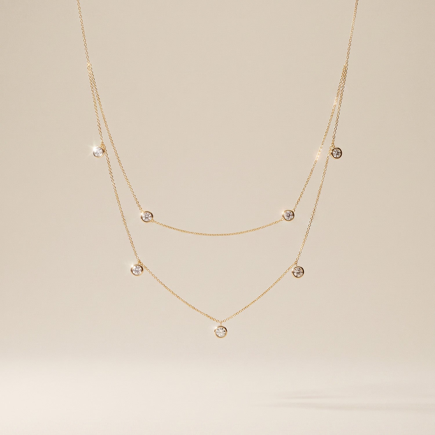 Two-layer yellow gold necklace with small round diamonds on a beige background
