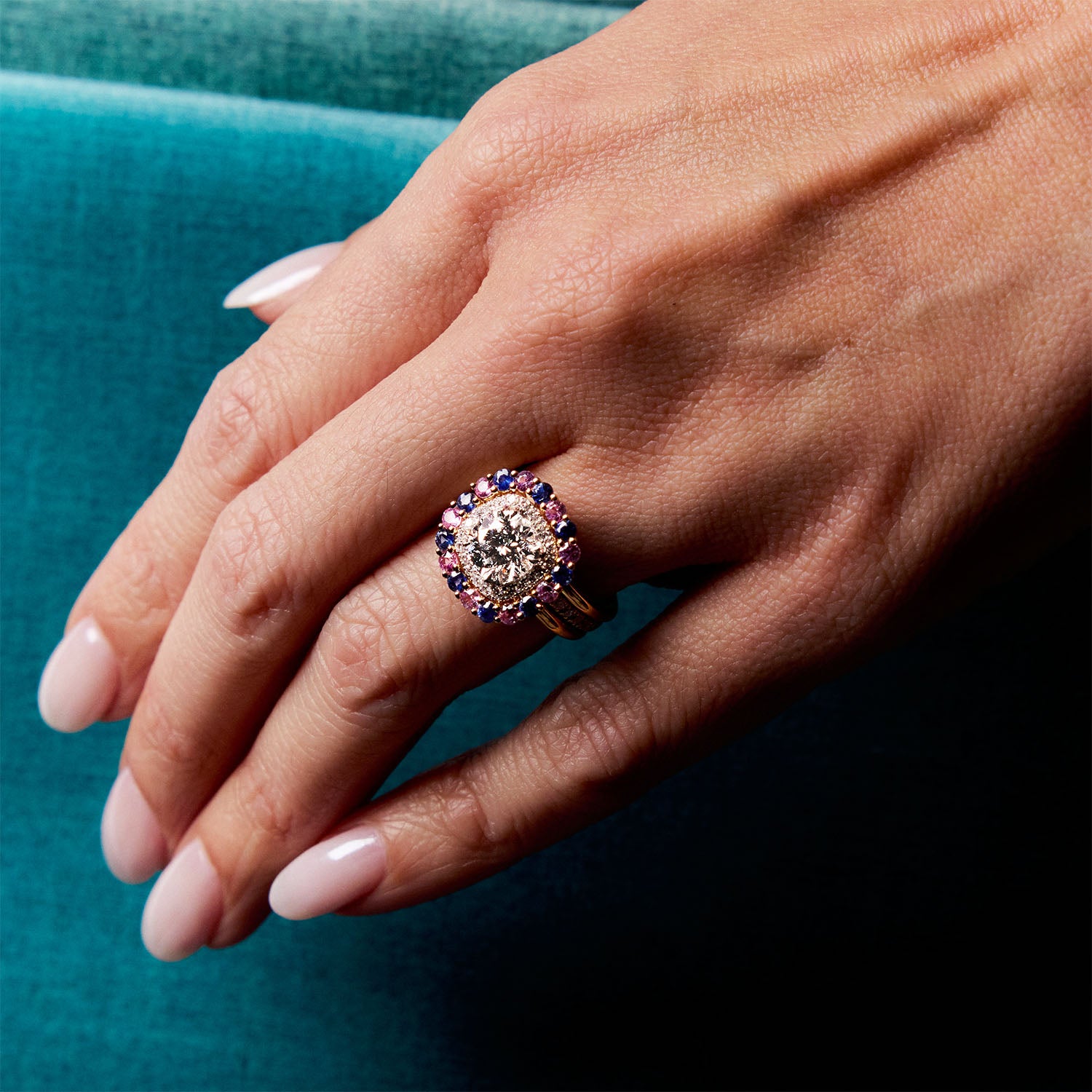 Diamond and sapphire halo ring in yellow gold, worn on hand