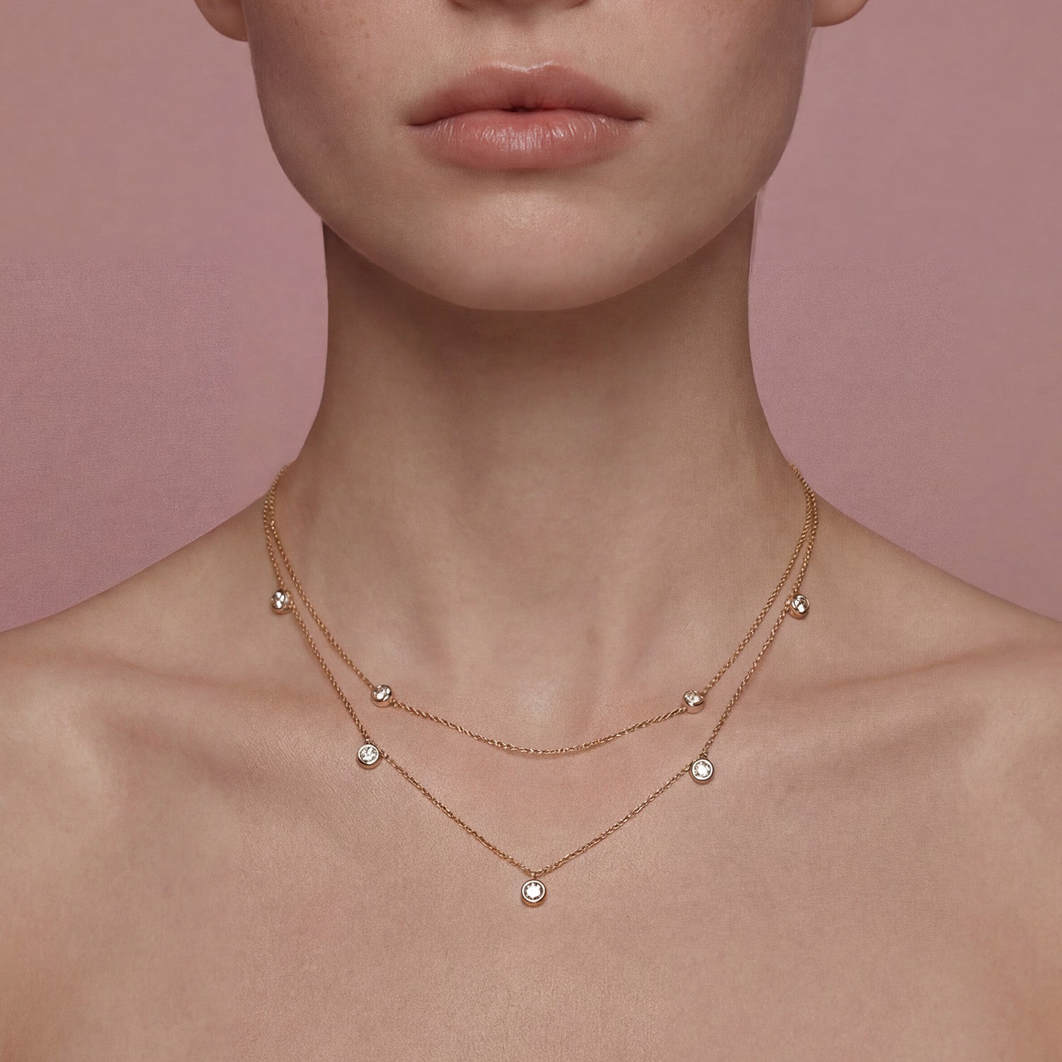 Close-up of a person wearing a delicate gold necklace with small round pendants against a pink background