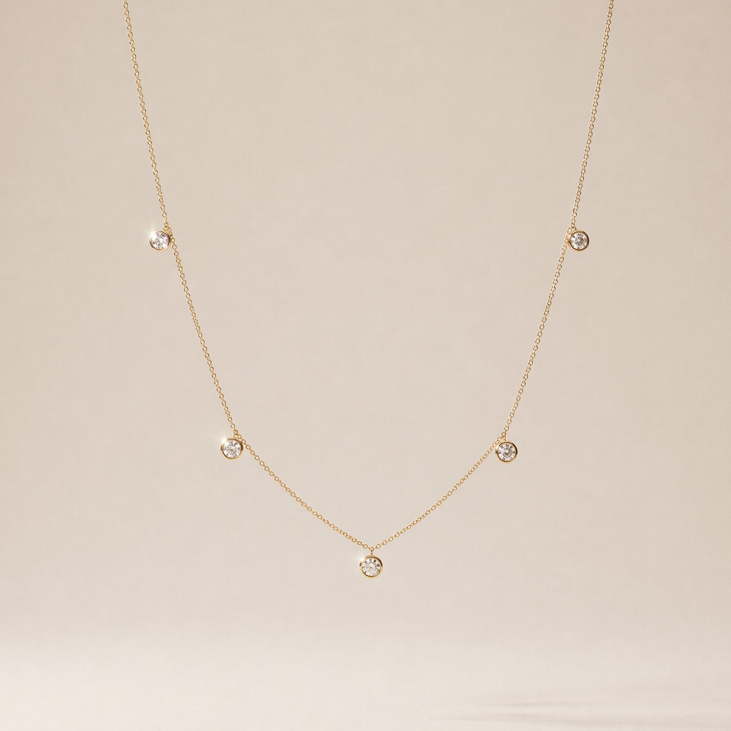 Delicate yellow gold necklace with small round diamond pendants on a beige background