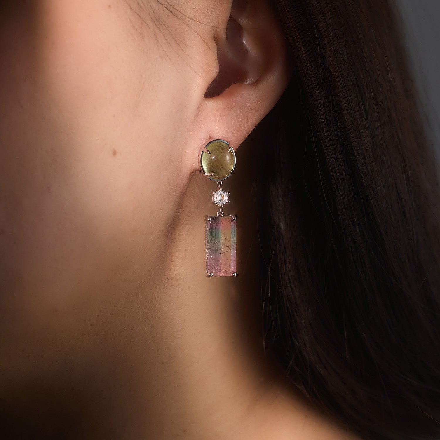 Close-up of a person wearing a colourful earring with pink and green colours, in tourmaline, diamond, aquamarine
